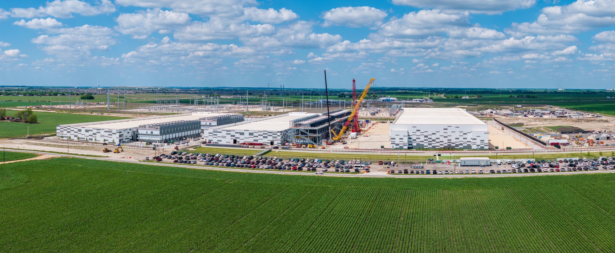 Construction cranes at work on a large computing campus beside open farmland