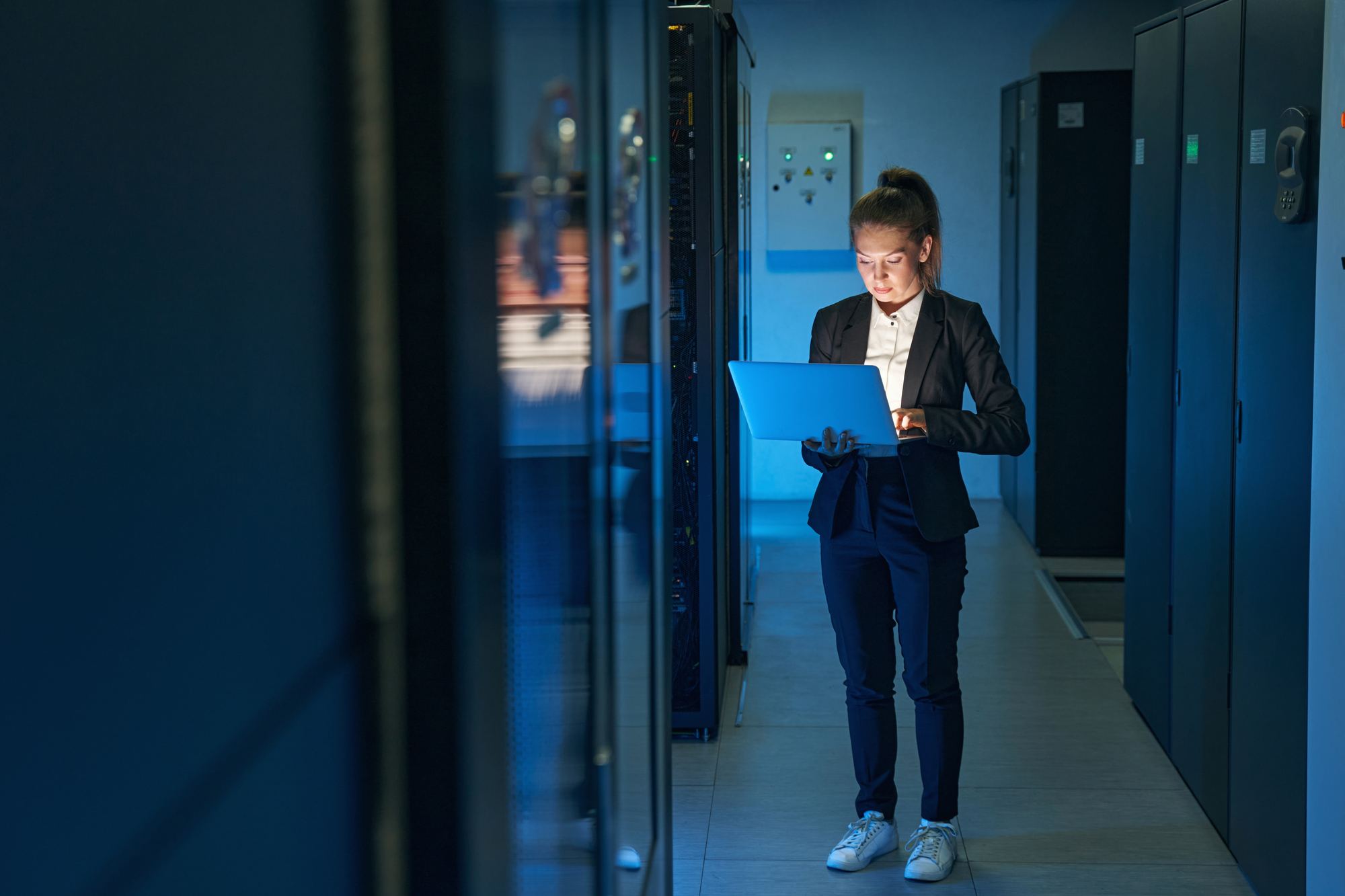 A technician reviewing a laptop in a dimly lit data center corridor